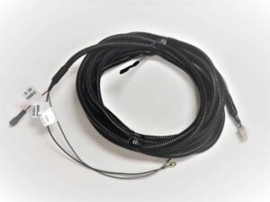 A coiled black electrical wiring harness with a protective sleeve, labeled wires, connectors, and a metal ring terminal, placed on a white surface.